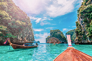 Longtailbåt i tropisk vik med höga klippor och soligt väder i Thailand.