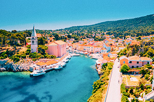 Färgglad kuststad i Kroatien med kyrktorn, båtar och grönskande kullar.