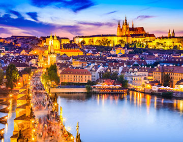Kvällsvy över Prag med Karlsbron och slottet upplyst ovanför floden Vltava.