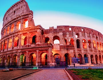 Colosseum i Rom lyses upp av kvällssol under en klarblå himmel.