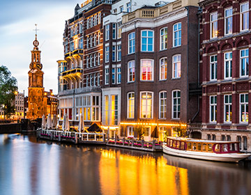  Historiska hus och båtar längs en stilla kanal i Amsterdam i kvällstid.