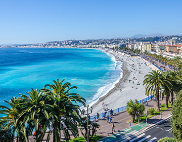 Strandpromenad i Nice med palmer, blått hav och solig strand.